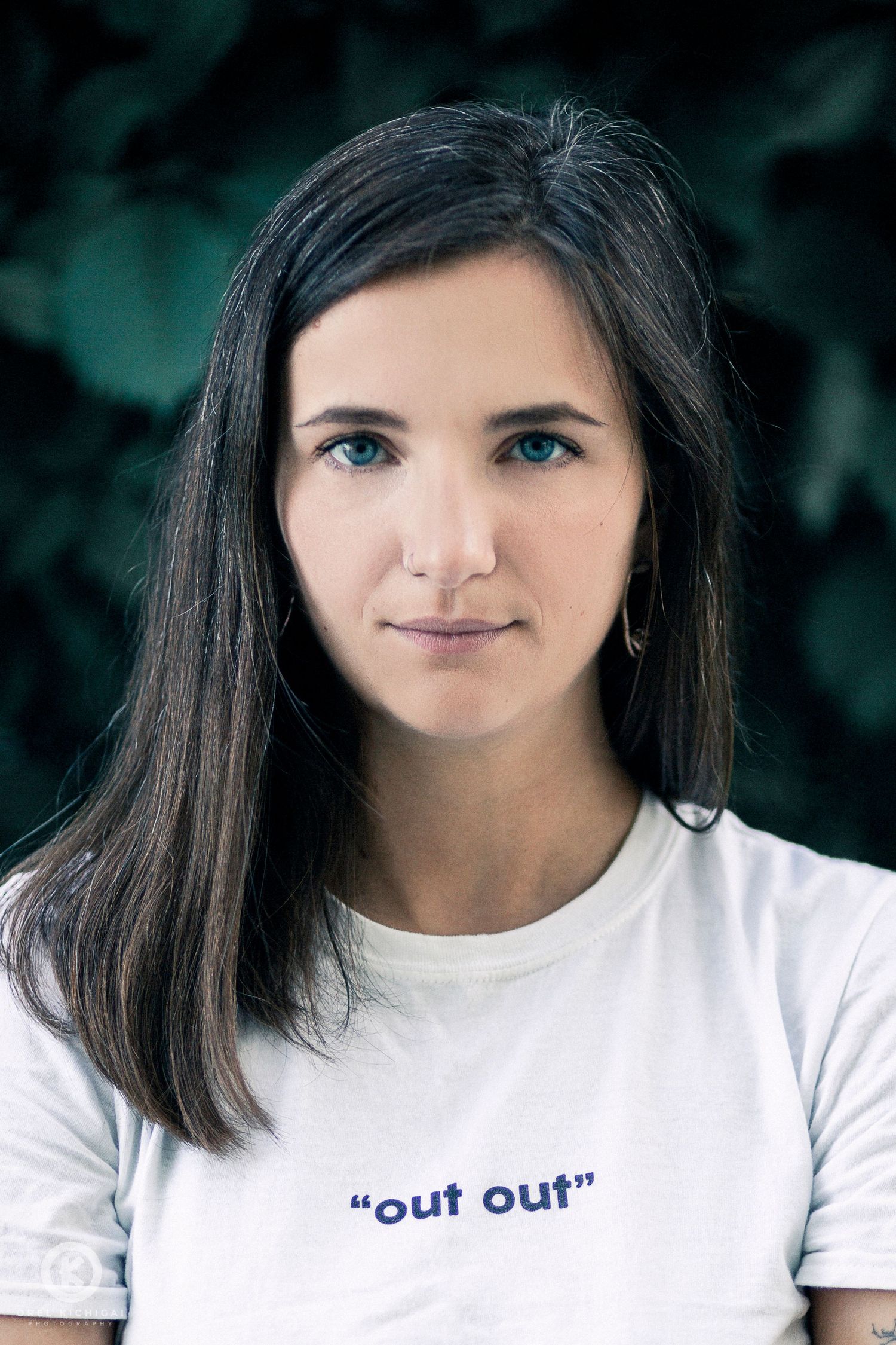 A portrait of someone wearing a white 'out out' t-shirt against a blurred green background.