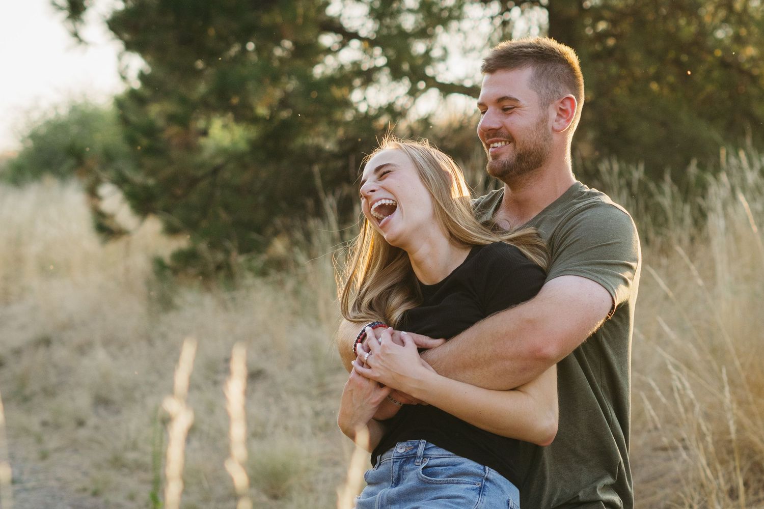 A couple shares a joyful embrace while laughing together in a sun-lit outdoor setting.