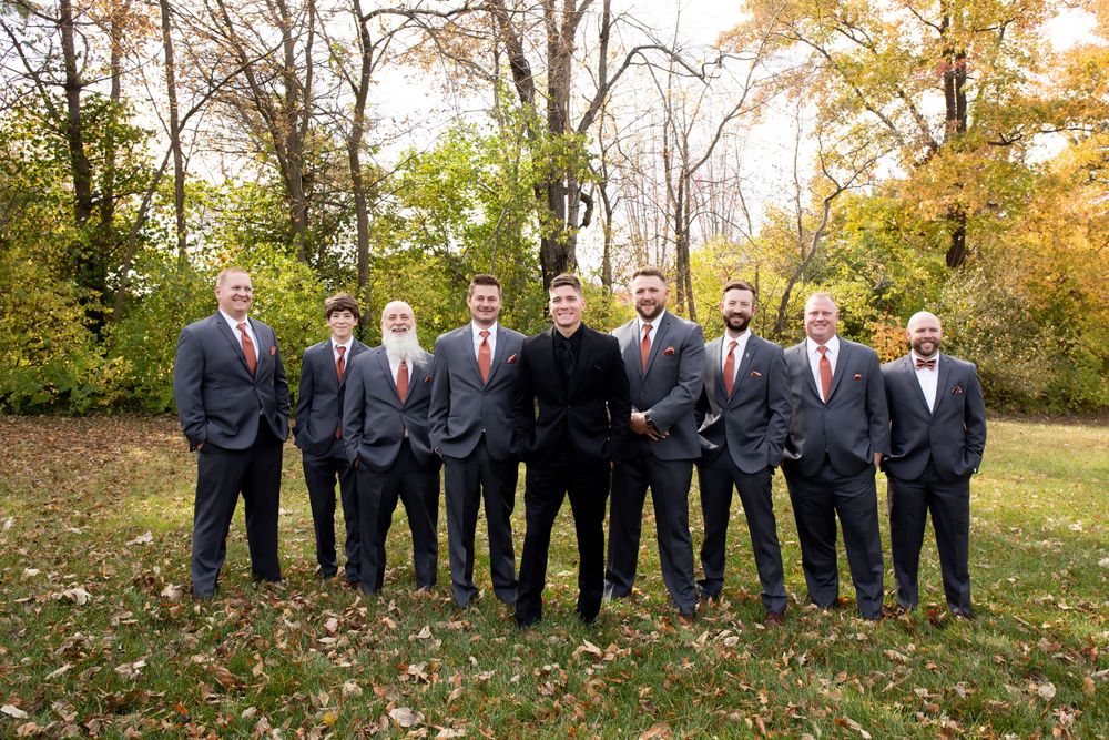 Group wearing matching navy suits poses outdoors in fall foliage.