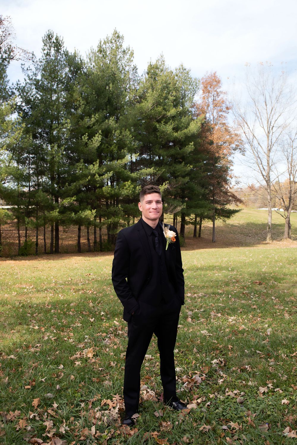 Solo formal portrait in a black suit against autumn trees and grass.