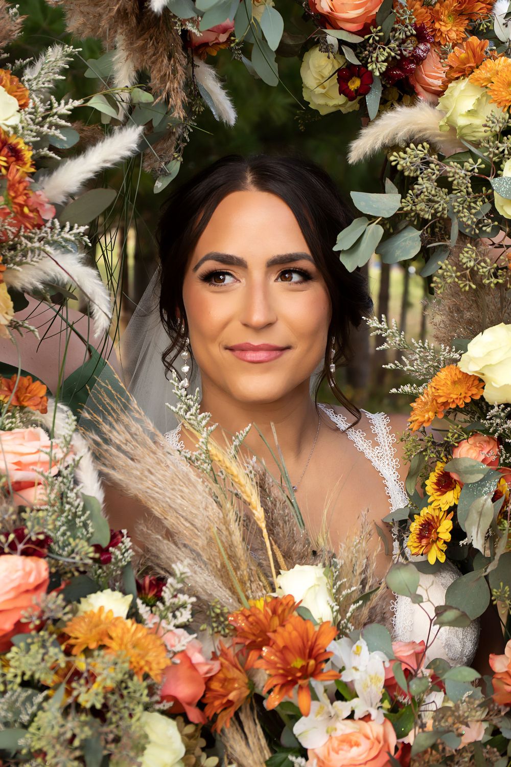 Bridal portrait surrounded by autumn floral arrangement with pampas grass and orange blooms.