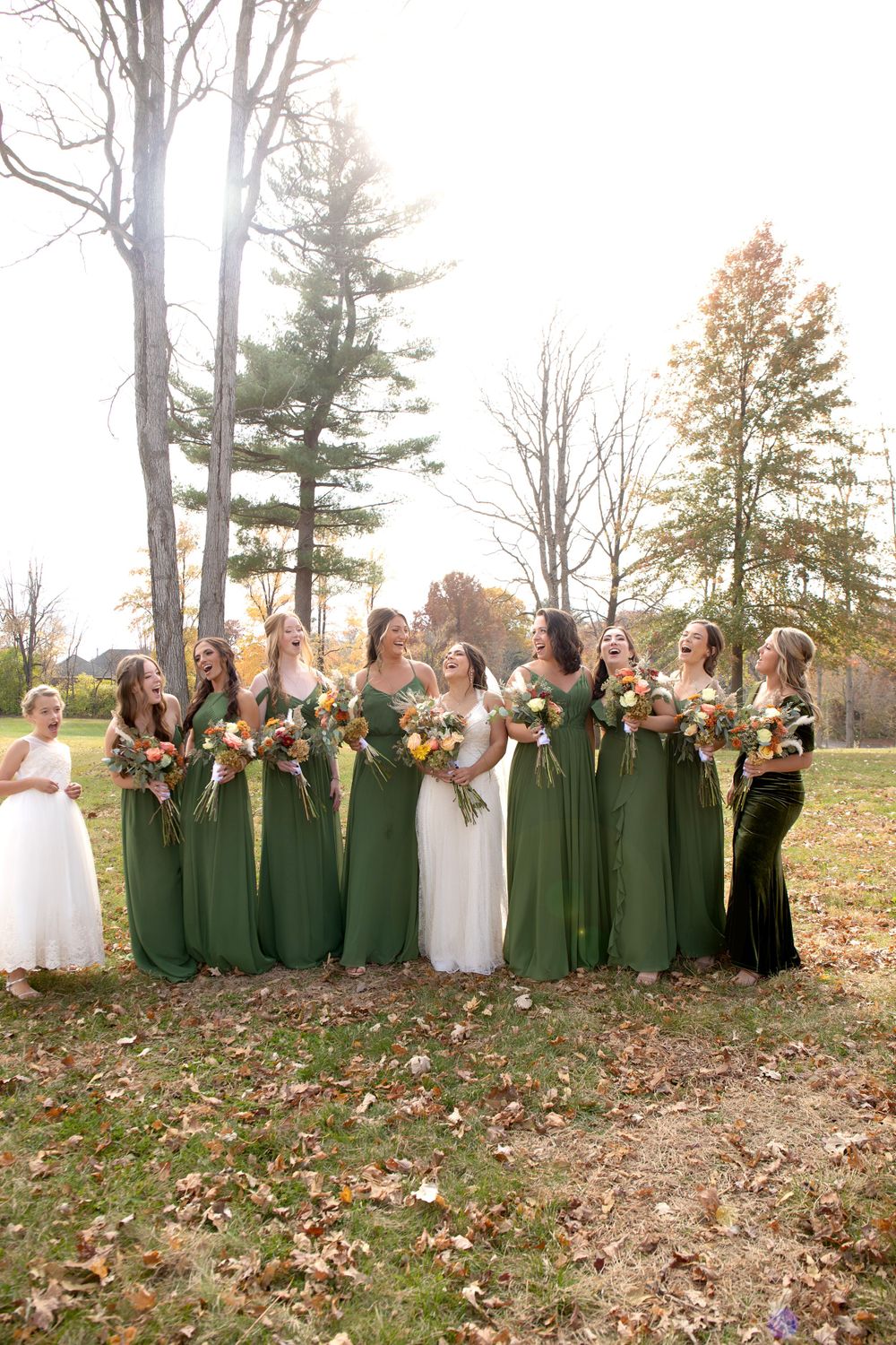 Wedding party in forest wearing emerald green dresses holding autumn bouquets.