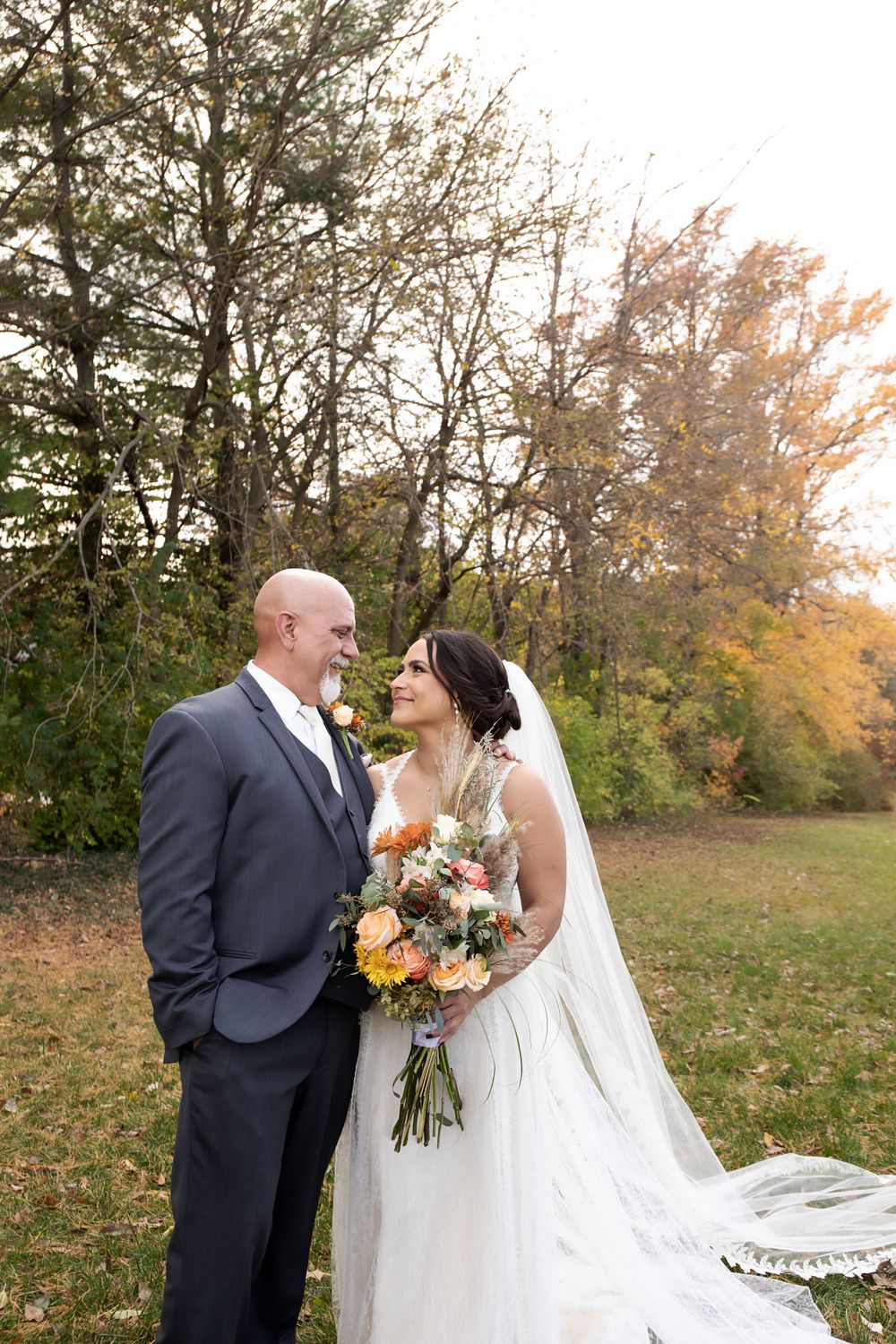 Newlyweds embrace outdoors with fall foliage and colorful bouquet.