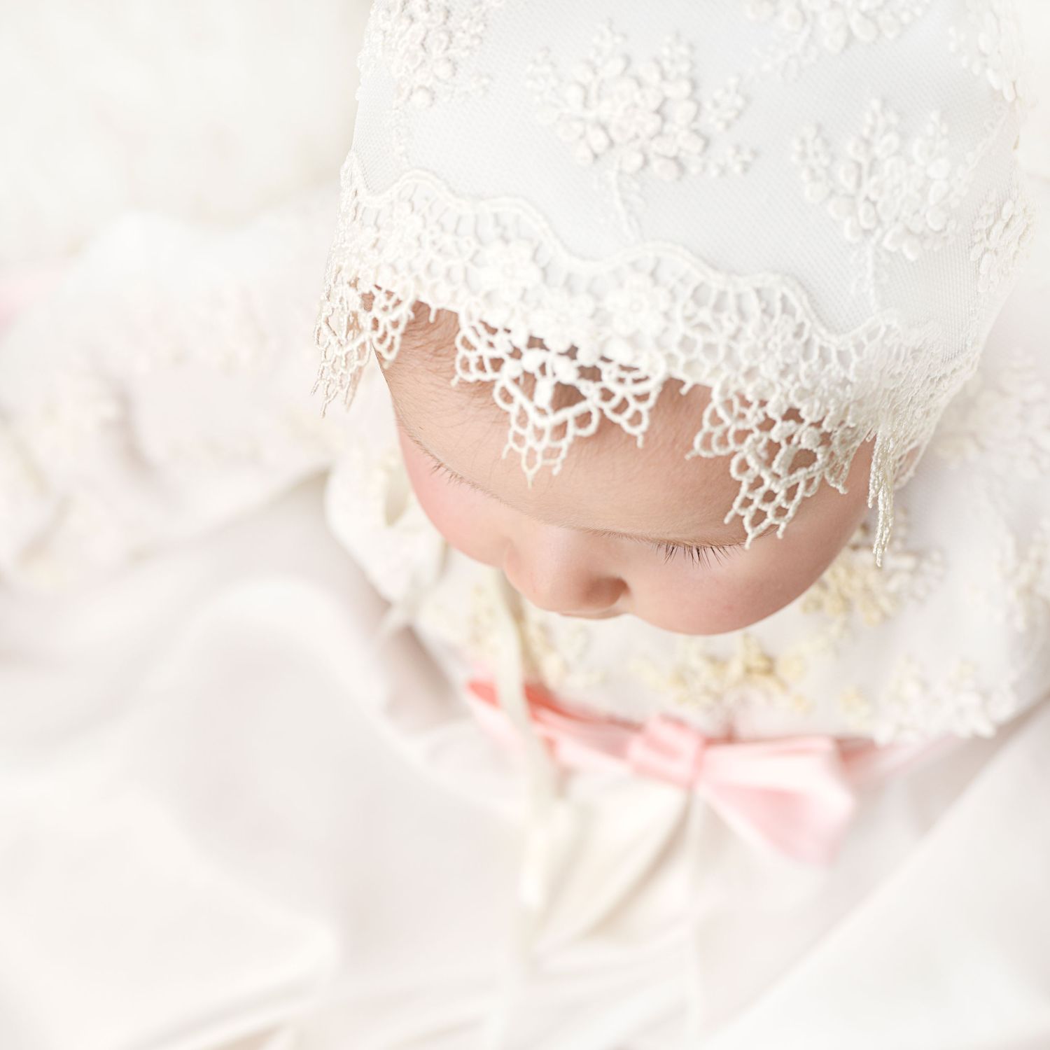 Close up of baby wearing vintage lace bonnet with pink bow detail.
