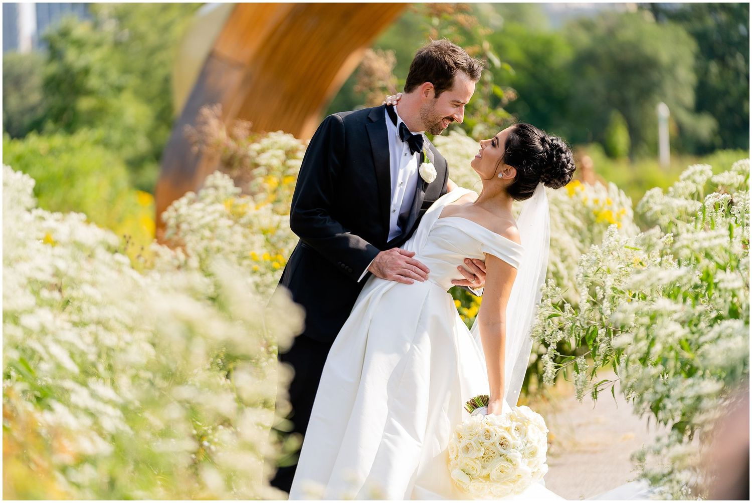 Romantic garden wedding portrait among white wildflowers on a sunny day.