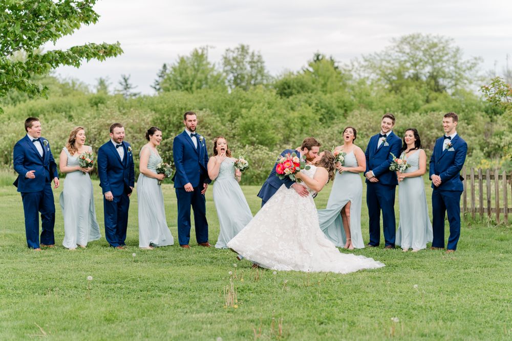Wedding party poses playfully on grass with bride and groom in center.