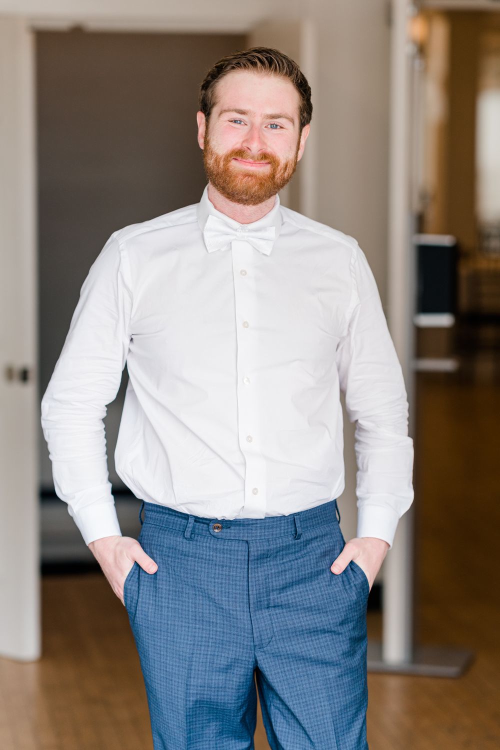 A groom in formal attire poses with hands in pockets before the ceremony.