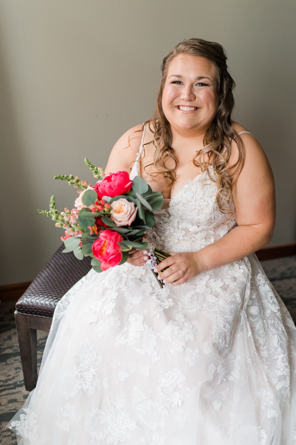 A radiant bride holds a vibrant pink and coral bouquet while seated in her wedding gown.