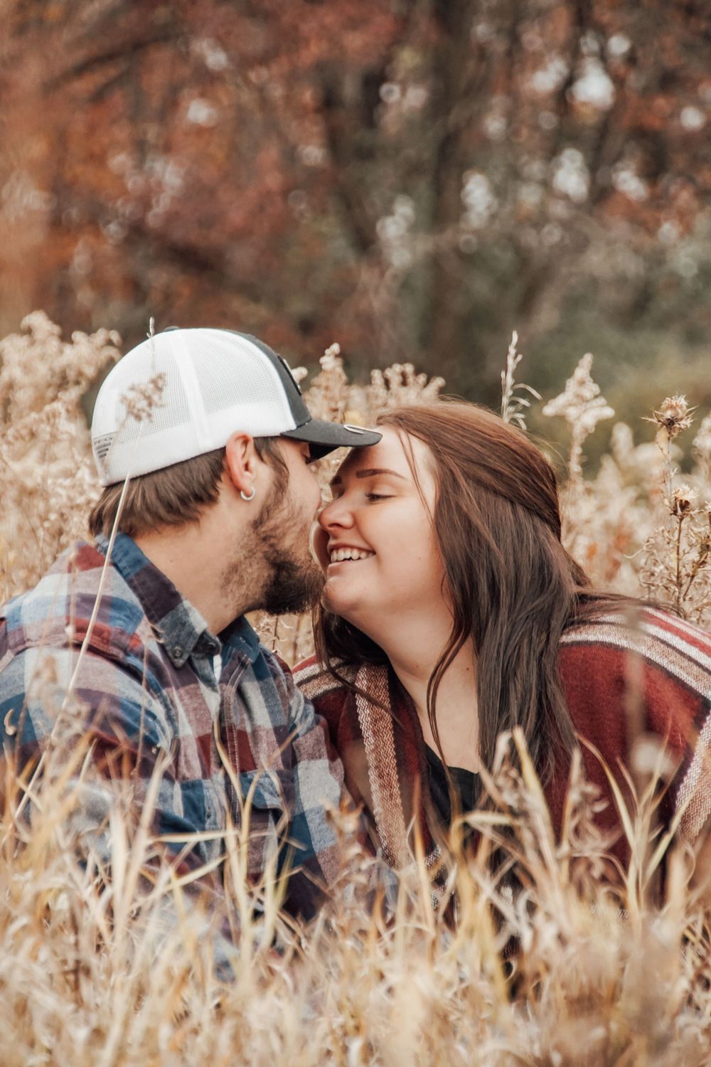 Romantic couple sharing intimate moment in tall autumn grass during sunset.