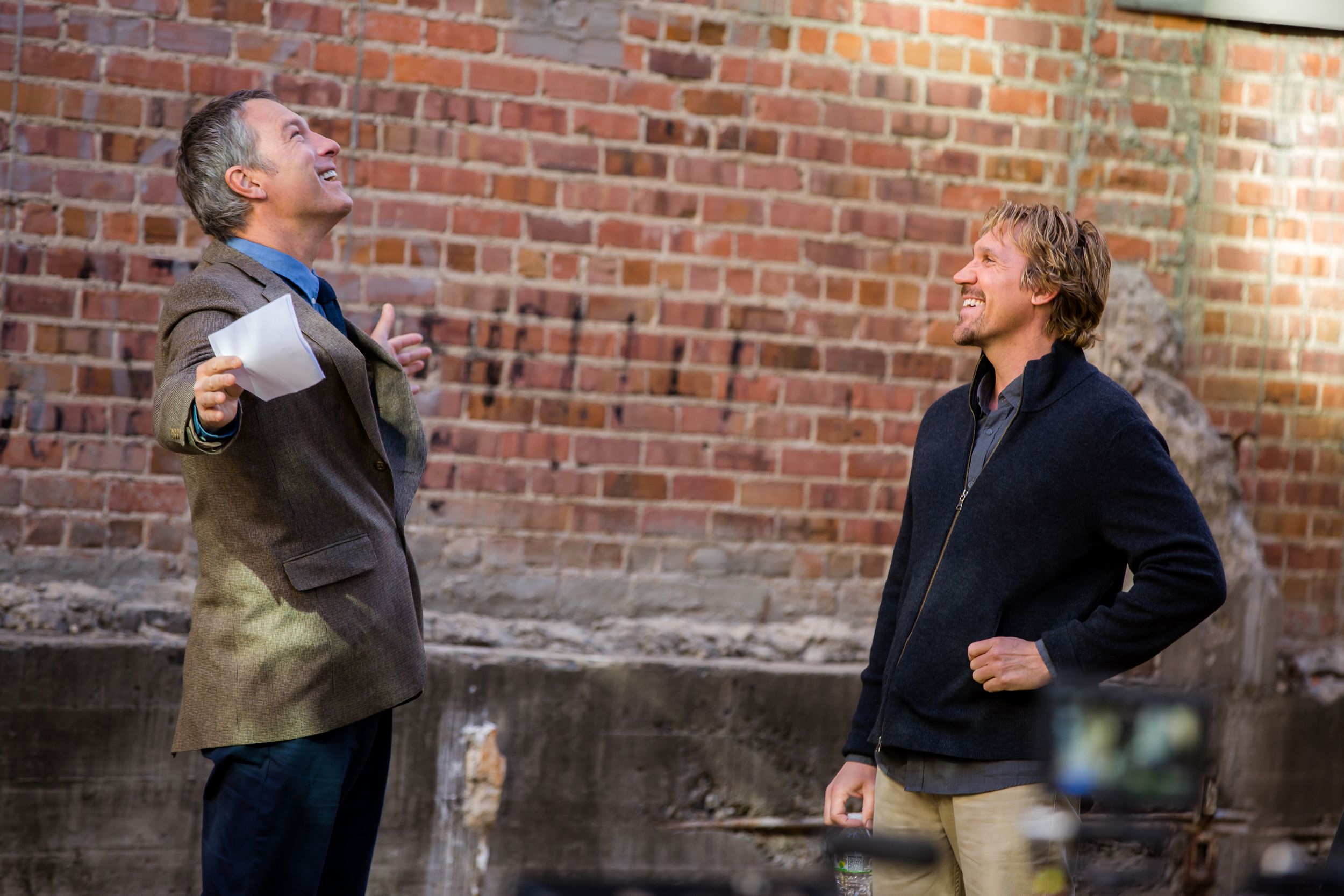 Film crew capturing footage against a rustic brick wall during an outdoor production.