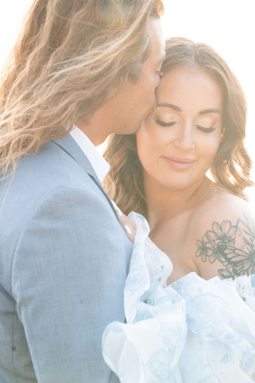 Tender wedding moment captured in soft dreamy light showing romantic couple embrace in formal attire.