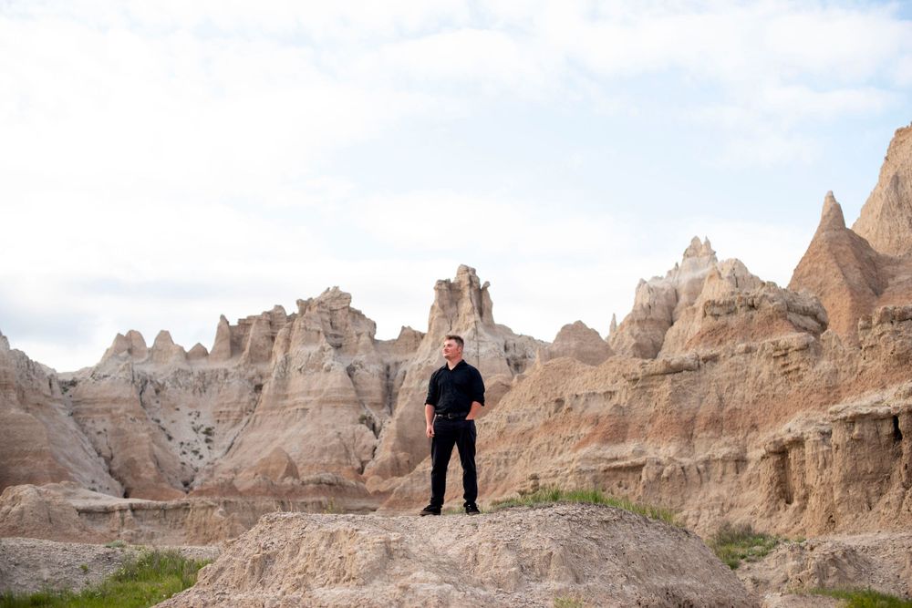 A silhouette stands atop rugged rock formations in Badlands National Park.
