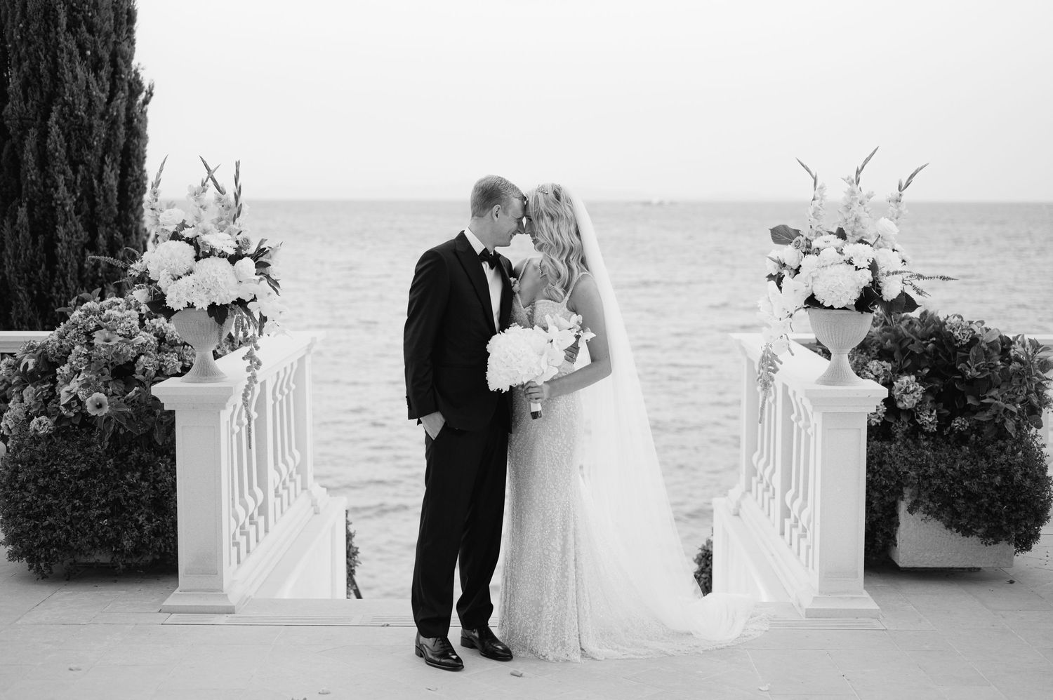 Black and white photo of romantic wedding ceremony moment with ocean backdrop.