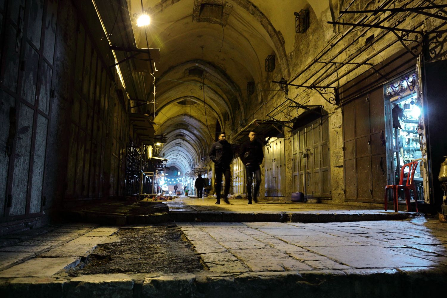 Historic arched corridor at night with illuminated shops and silhouetted figures.
