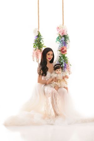 Mother and baby portrait on floral swing with hanging pink and blue flowers.