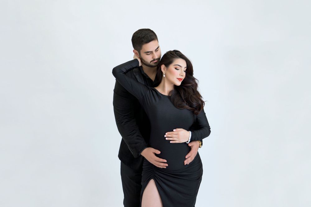 Intimate maternity portrait with couple in black outfits against white background.