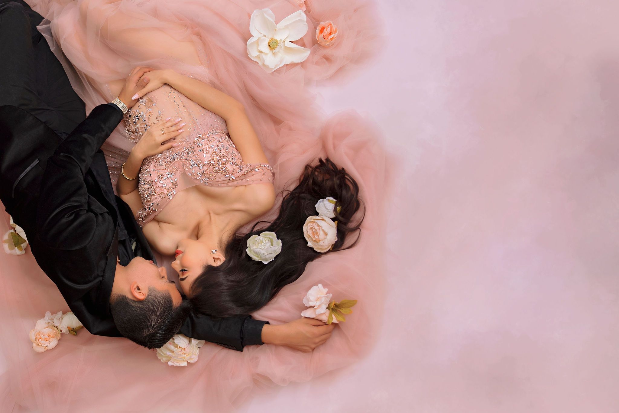 Ethereal overhead maternity photo with scattered white and pink flowers.