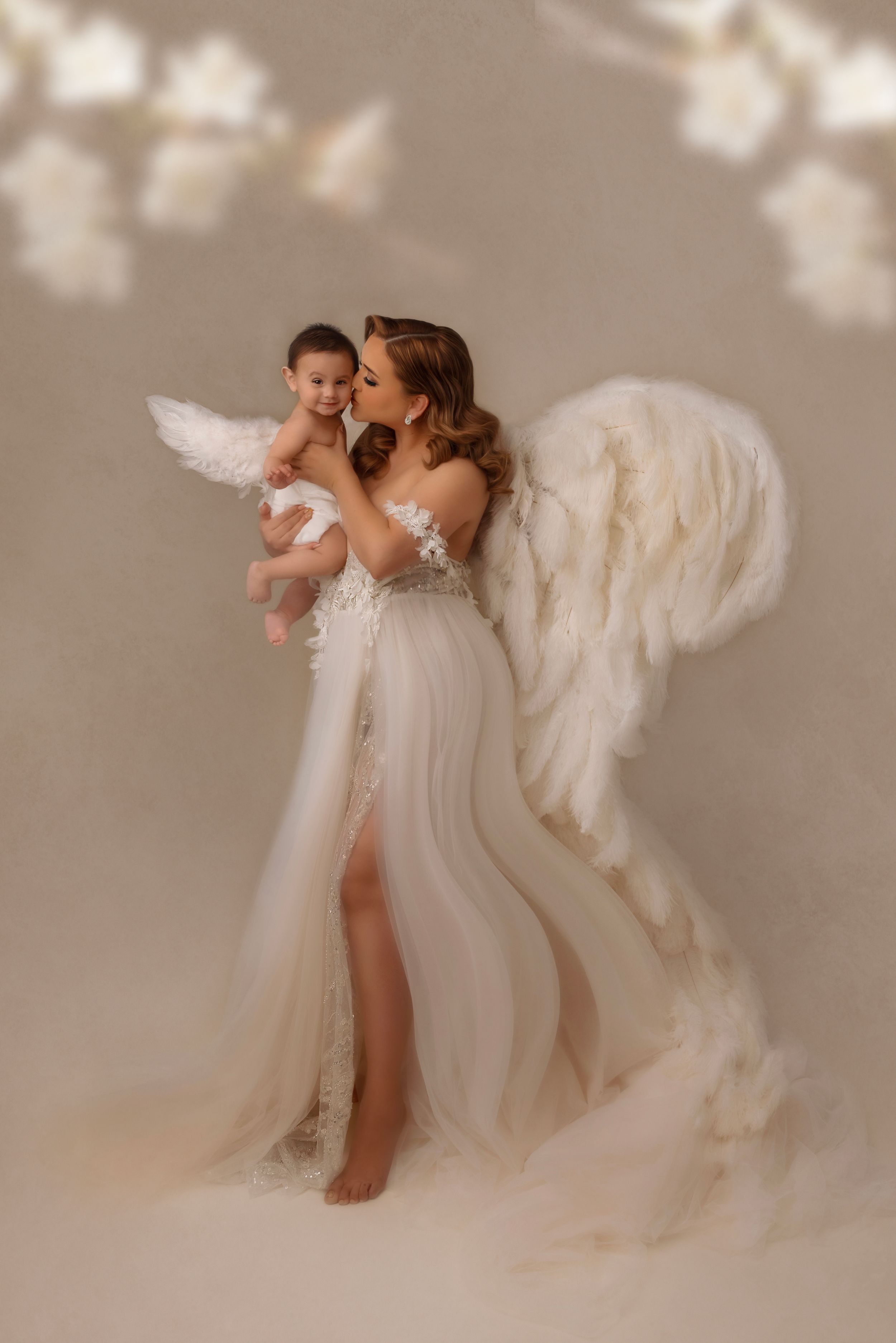 Ethereal studio portrait with flowing white gown and angel wings against a neutral background.