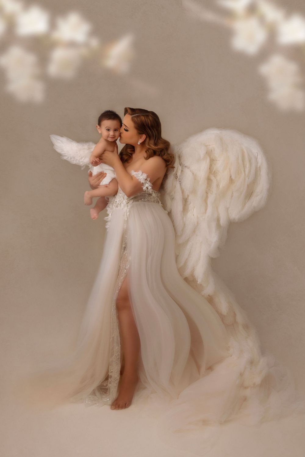 Ethereal studio portrait with flowing white gown and angel wings against a neutral background.
