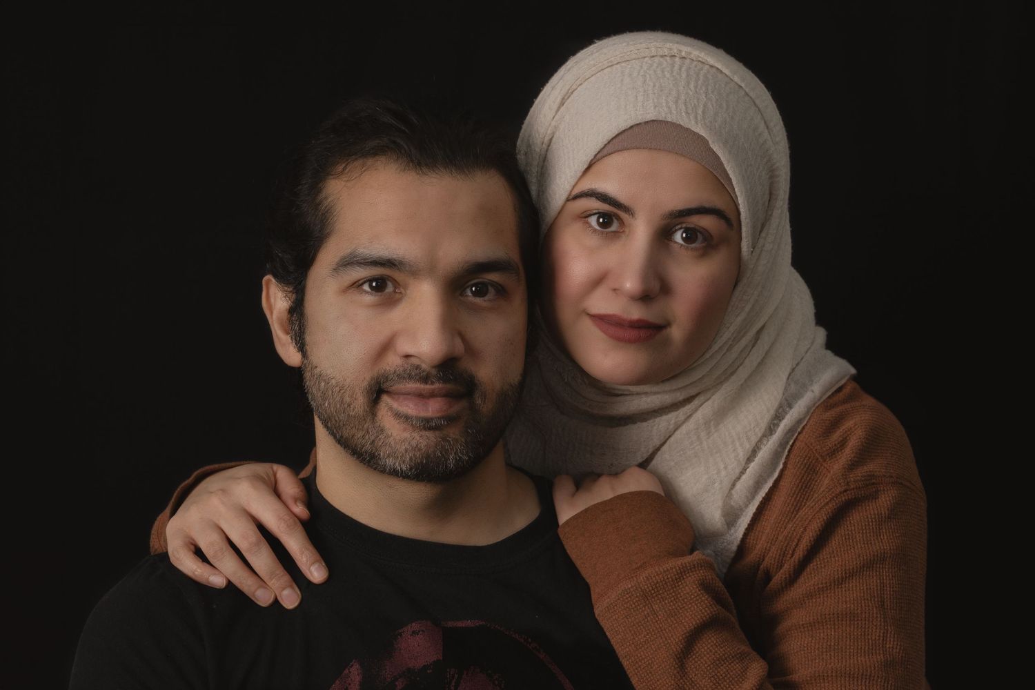 Couple poses for romantic portrait against dark background.