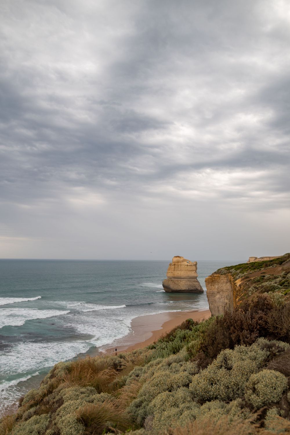 Moody seascape with limestone cliffs and crashing waves under cloudy skies.