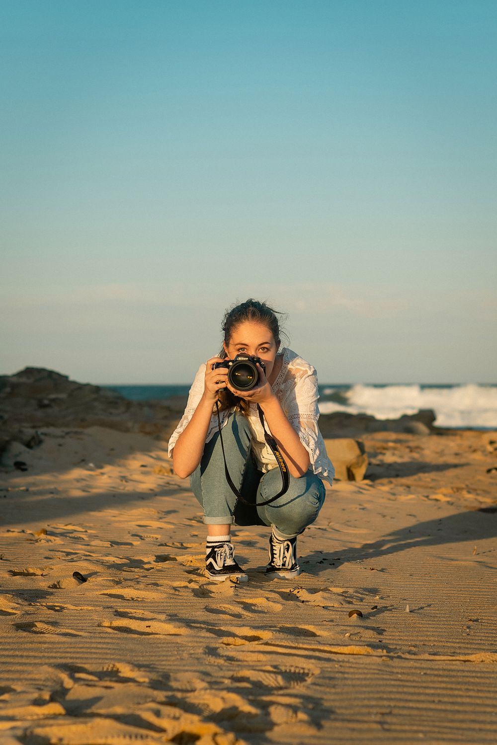 Photographer crouching on sandy beach taking photos during golden hour.