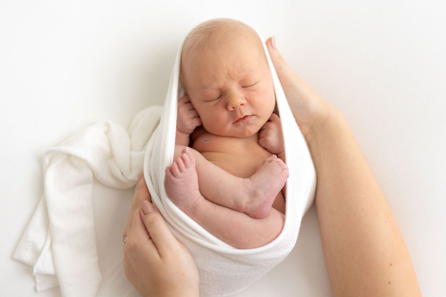 A peaceful sleeping newborn cradled in white fabric during a studio photography session.