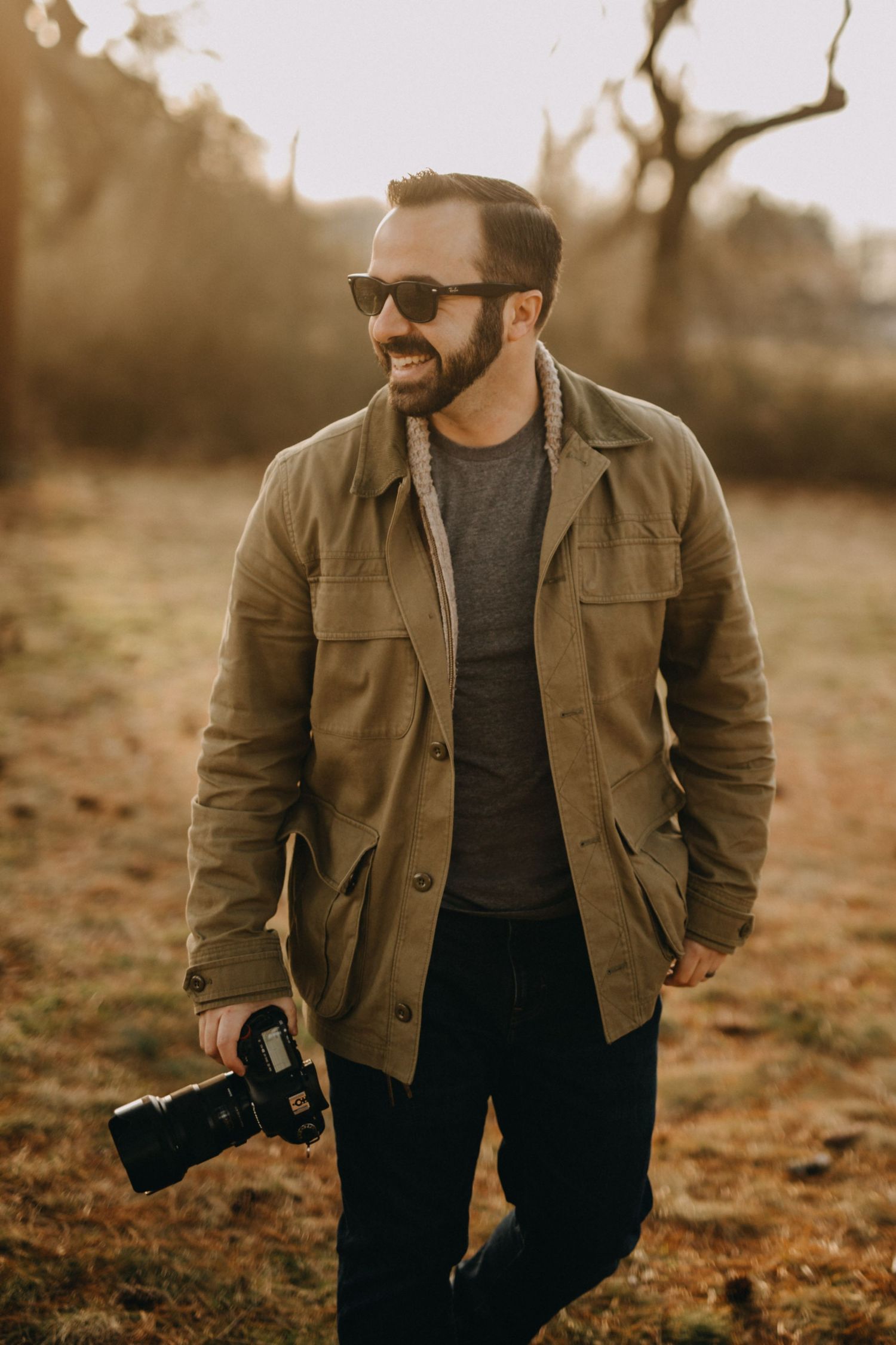 Professional photographer in brown jacket holding camera during golden hour shoot.