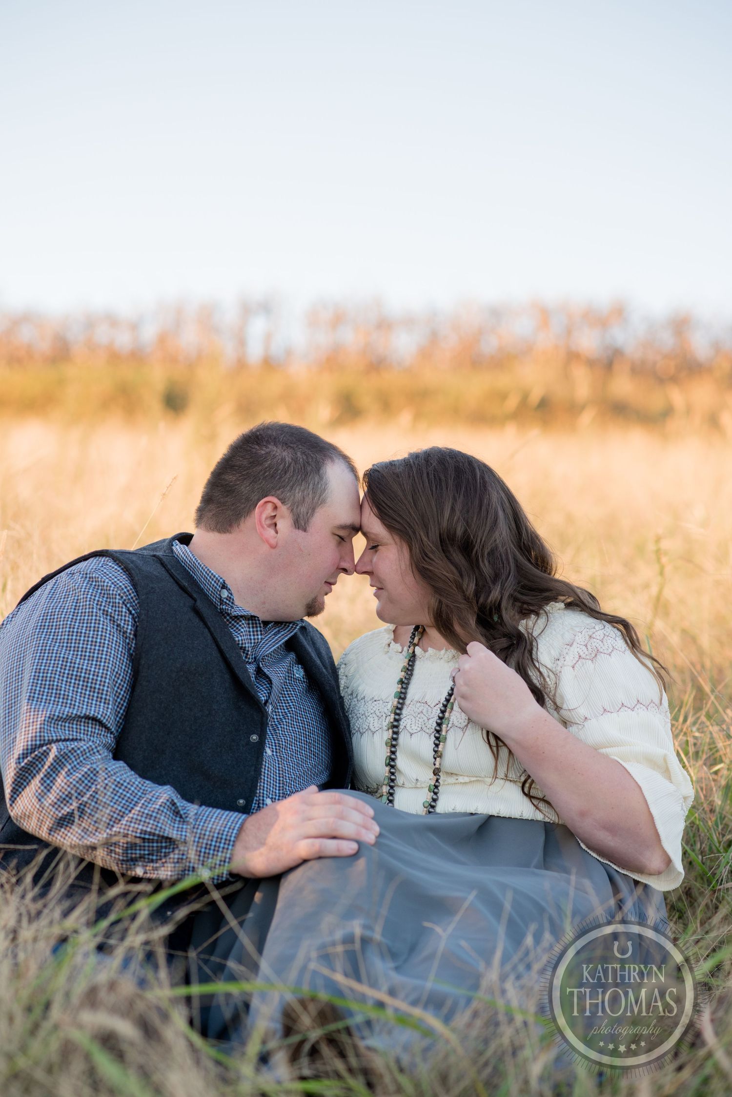 An intimate portrait of a couple sitting close together in a sunlit autumn field.
