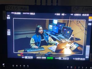 Camera monitor display showing film set with computer workstations.