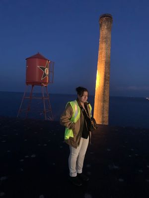 Production assistant in yellow jacket standing by illuminated tower and red water tank at dusk.