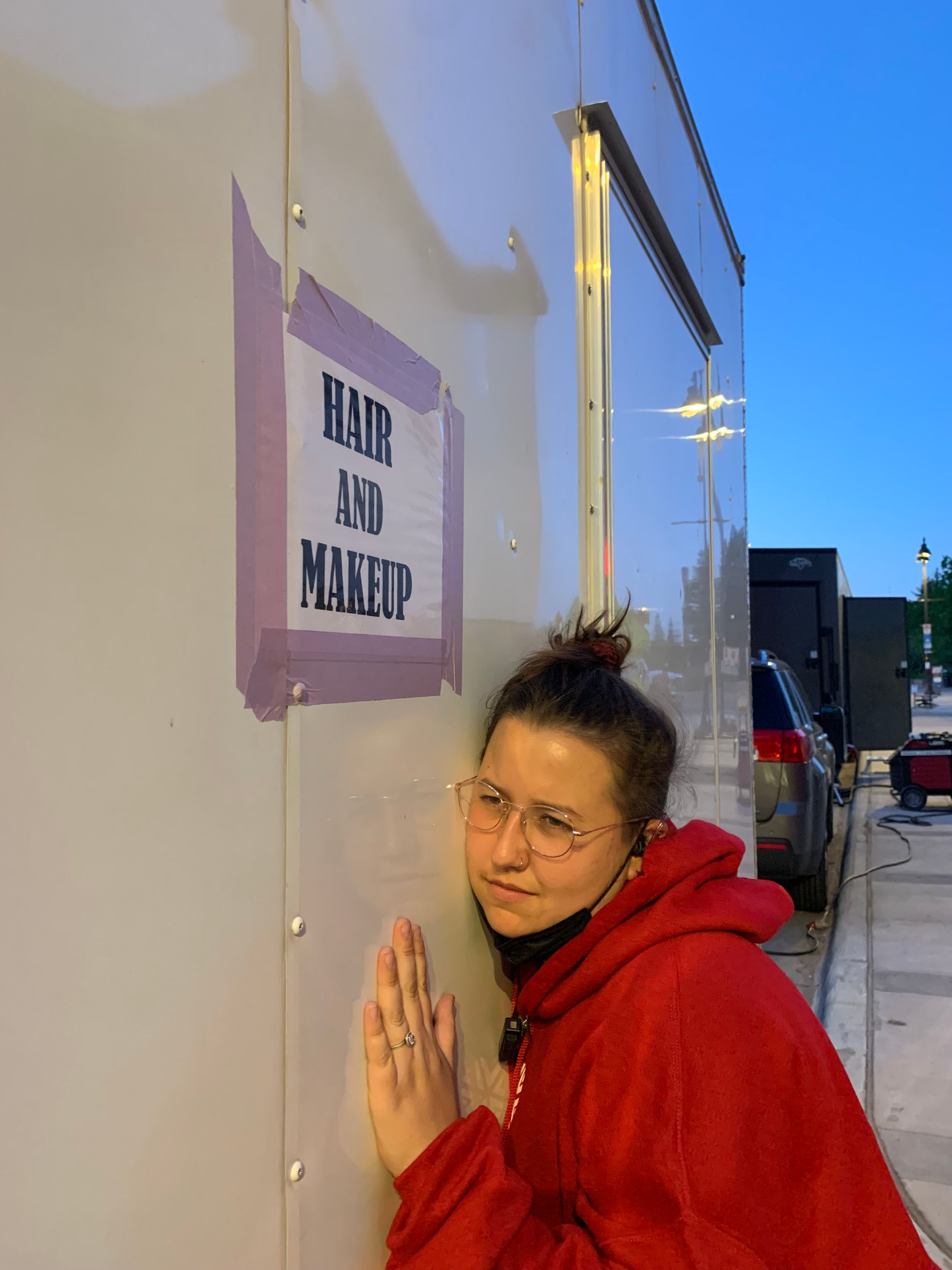 Production Assistant next to Hair and makeup sign mounted on white trailer wall.