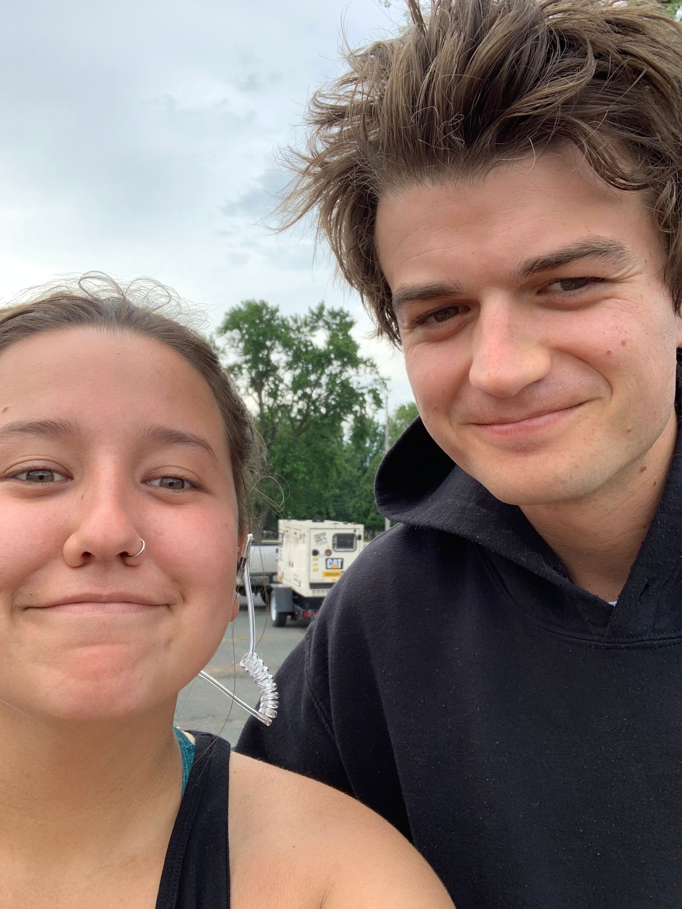 Outdoor selfie with Joe Keery taken in overcast weather with parked vehicles in background.