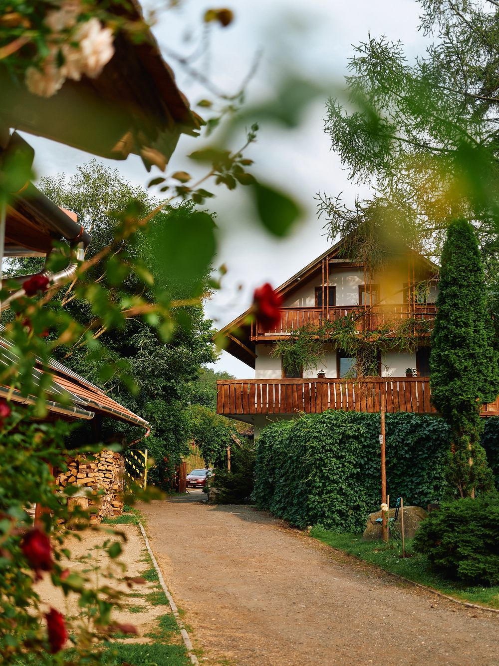 Rustic wooden lodge with balcony nestled among green trees and garden path.