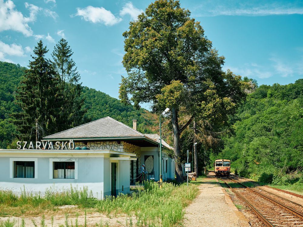 Rural train station building with 'Szklarska' sign surrounded by mountain forest.