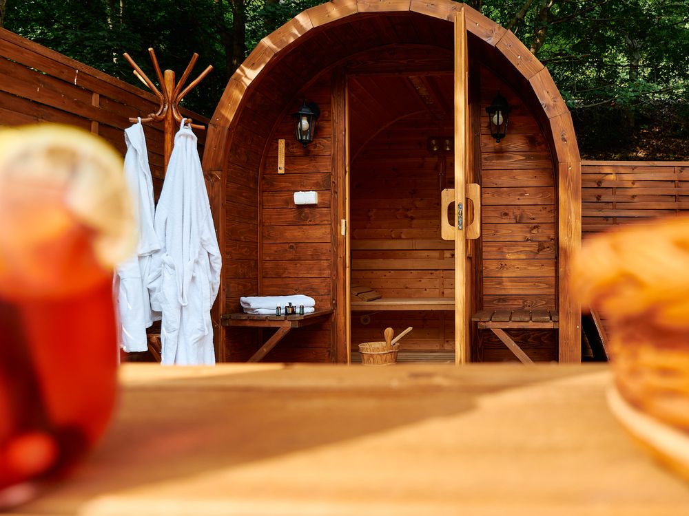 Wooden barrel sauna exterior with white robes hanging outside and drinks in the foreground.