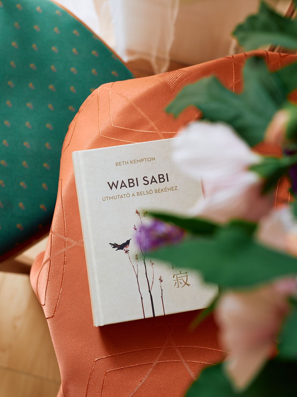 Wabi Sabi book on coral colored surface with green plants in soft focus.