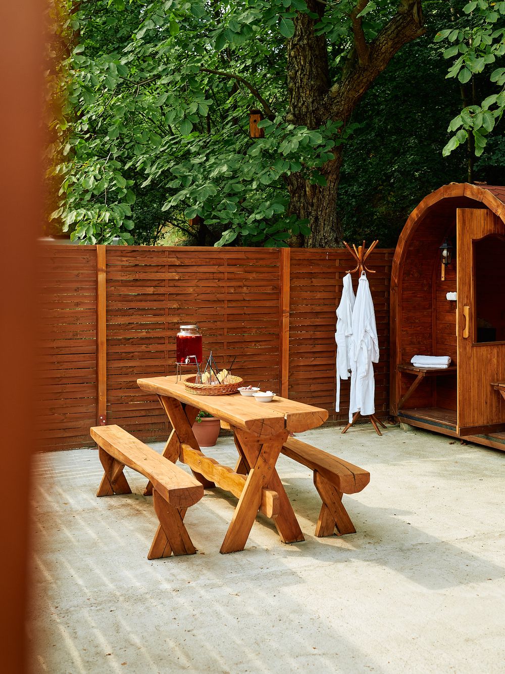 Rustic wooden picnic table with benches and white robes hanging near a sauna entrance.