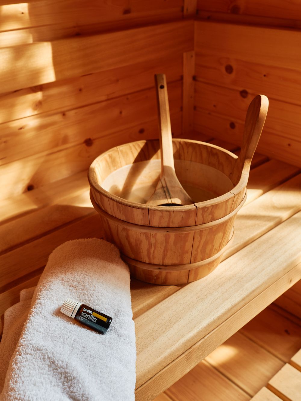 Wooden sauna bucket and white towel with thermometer in traditional Finnish sauna setting.