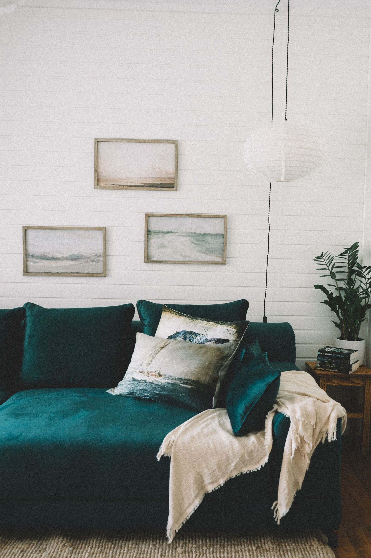 Emerald green velvet sofa with coastal artwork and throw blanket in modern living room.