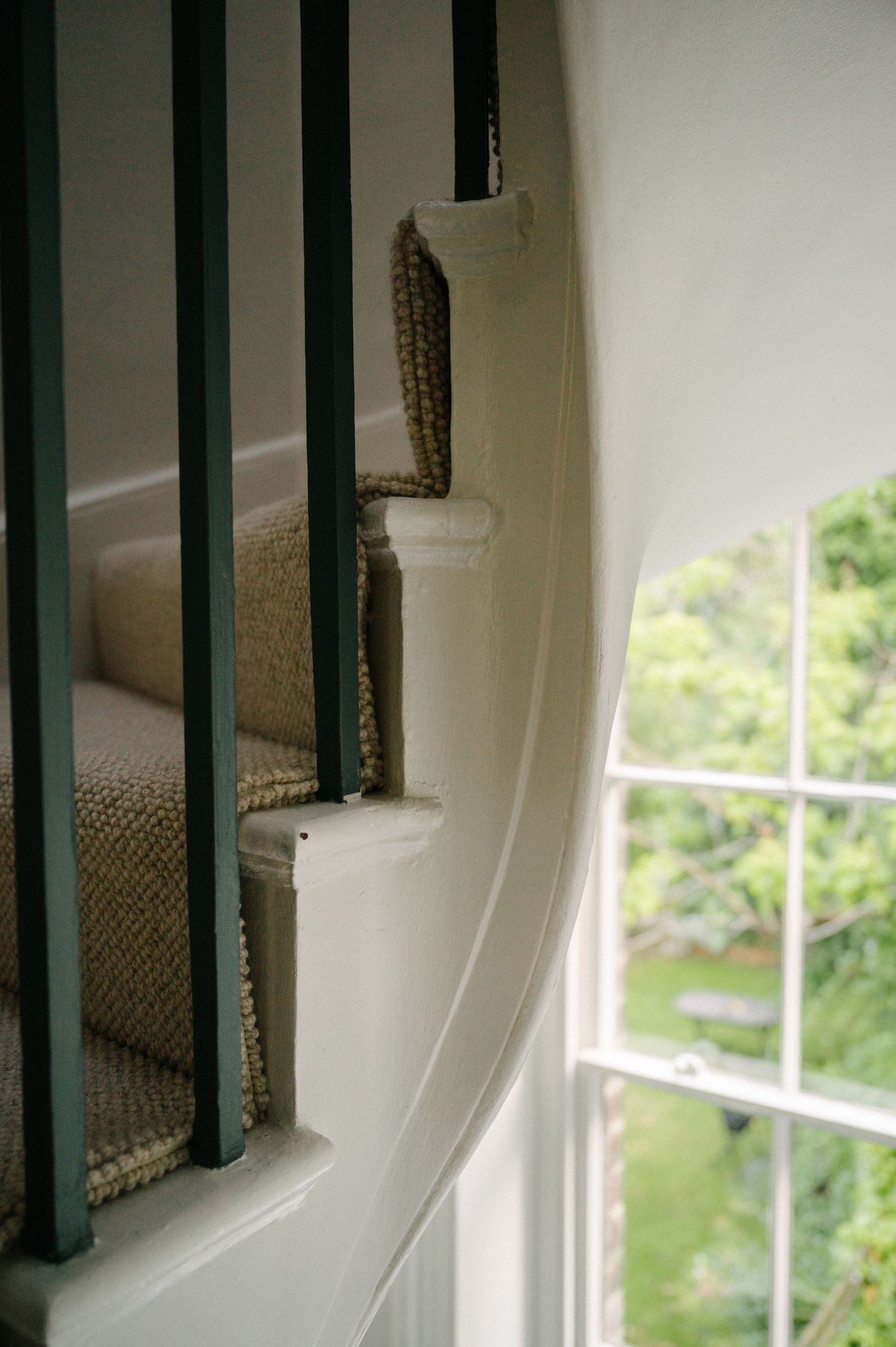 Carpeted stairs with dark railings beside window overlooking green outdoor scenery.