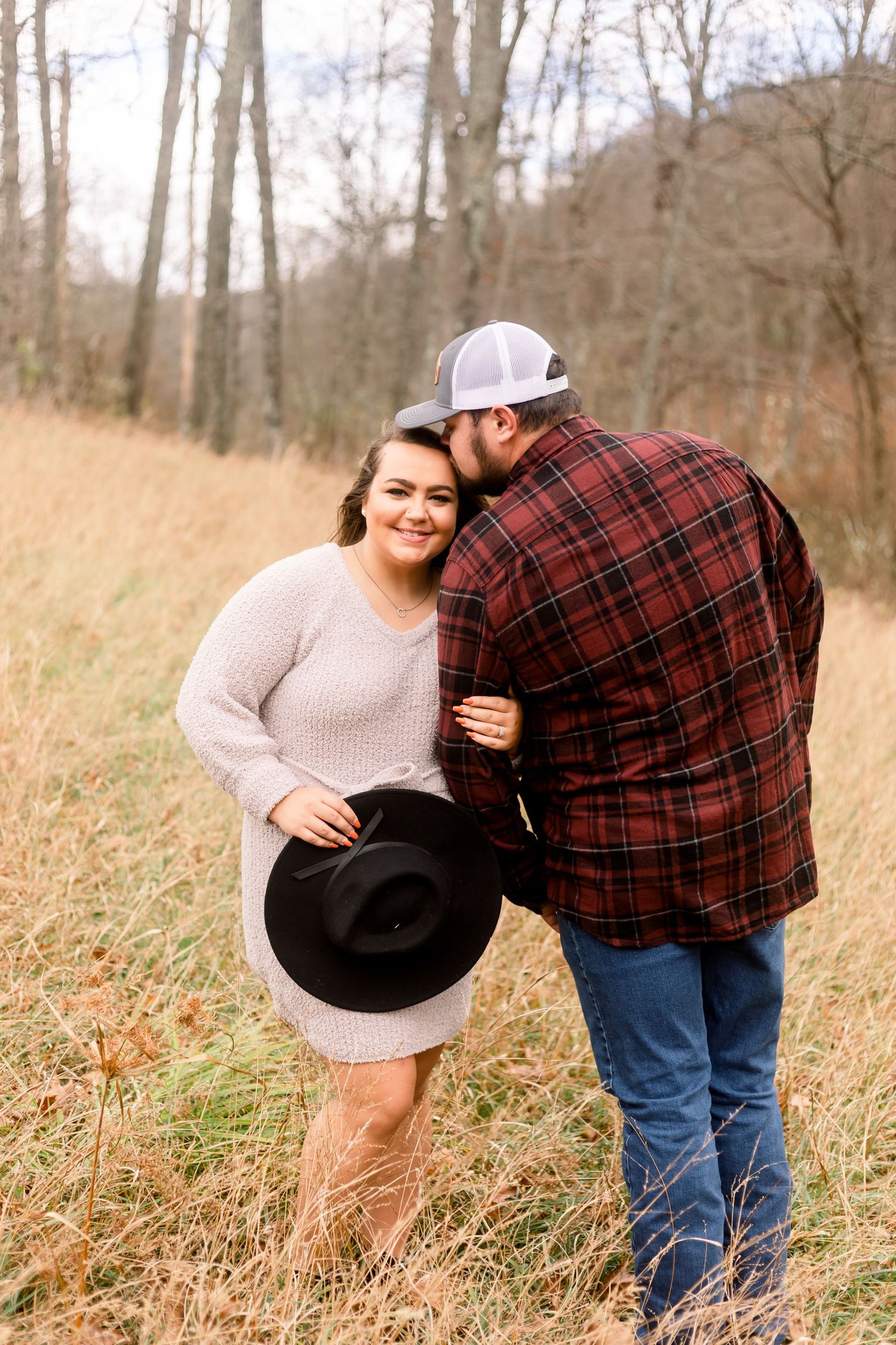 A playful moment captured between a couple in casual attire near tall grass and trees.