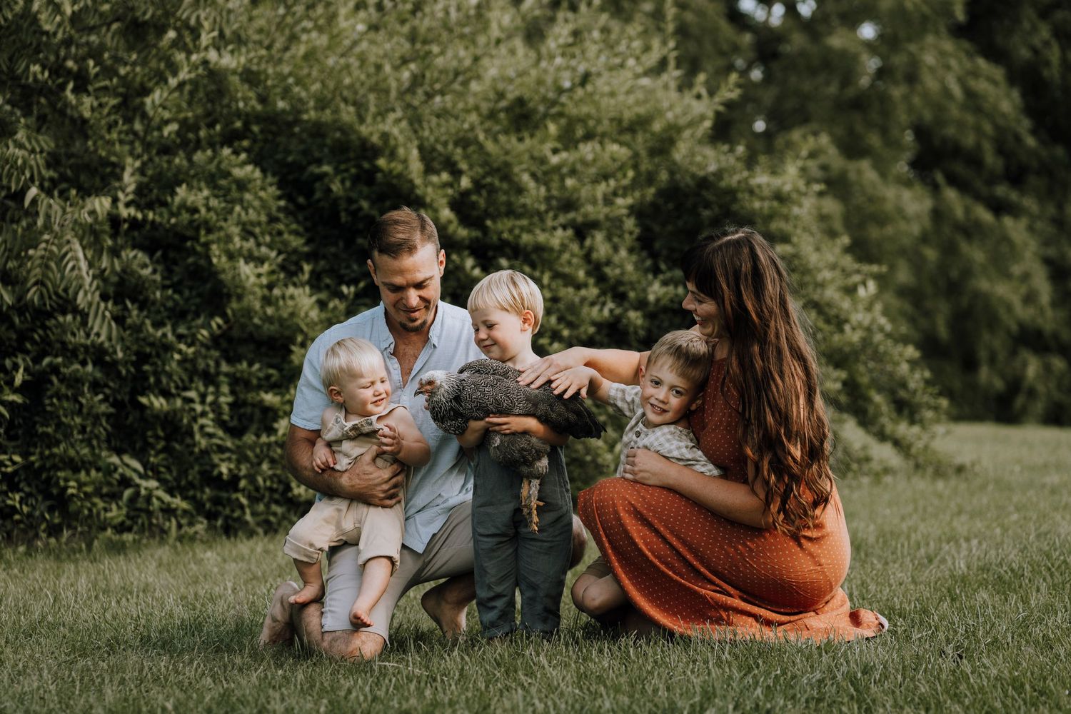 Family sitting together on grass while playing with chickens on a sunny day.