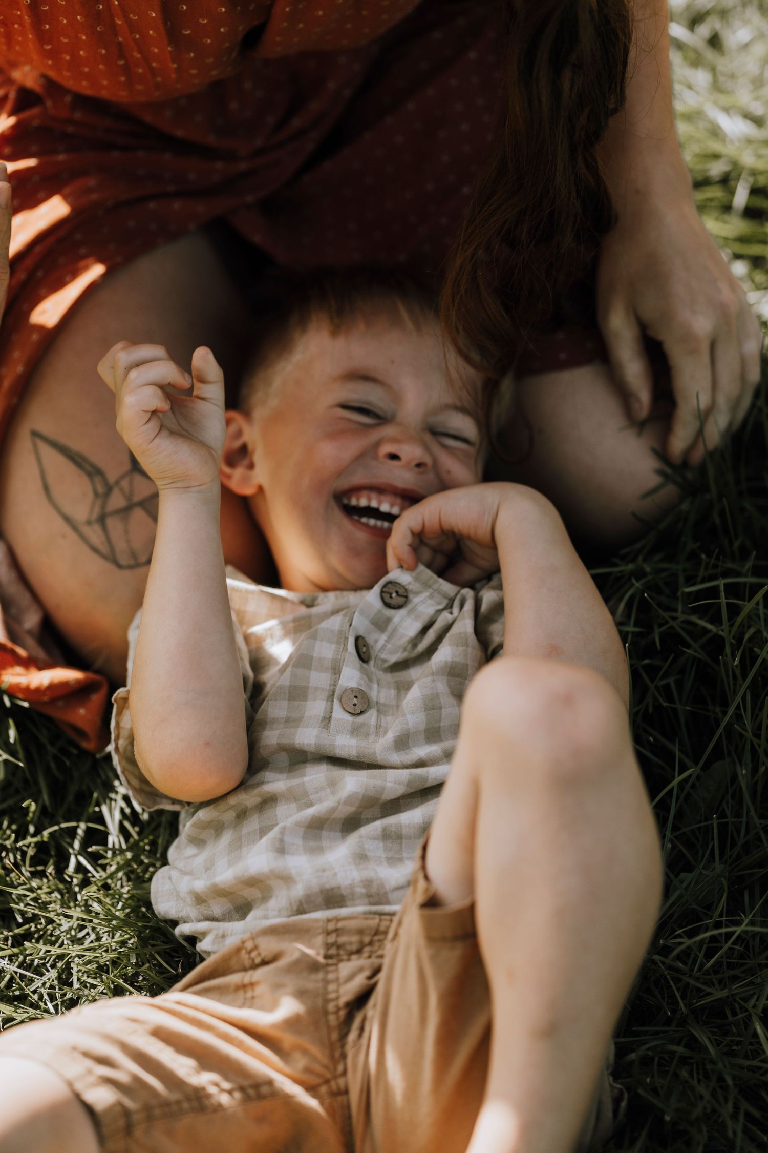 Child lying in grass laughing joyfully while playing outdoors.