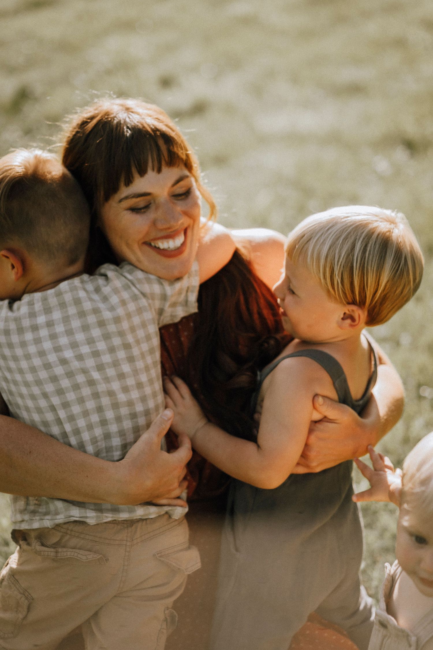A heartwarming outdoor family portrait showing genuine laughter and embraces in golden sunlight.