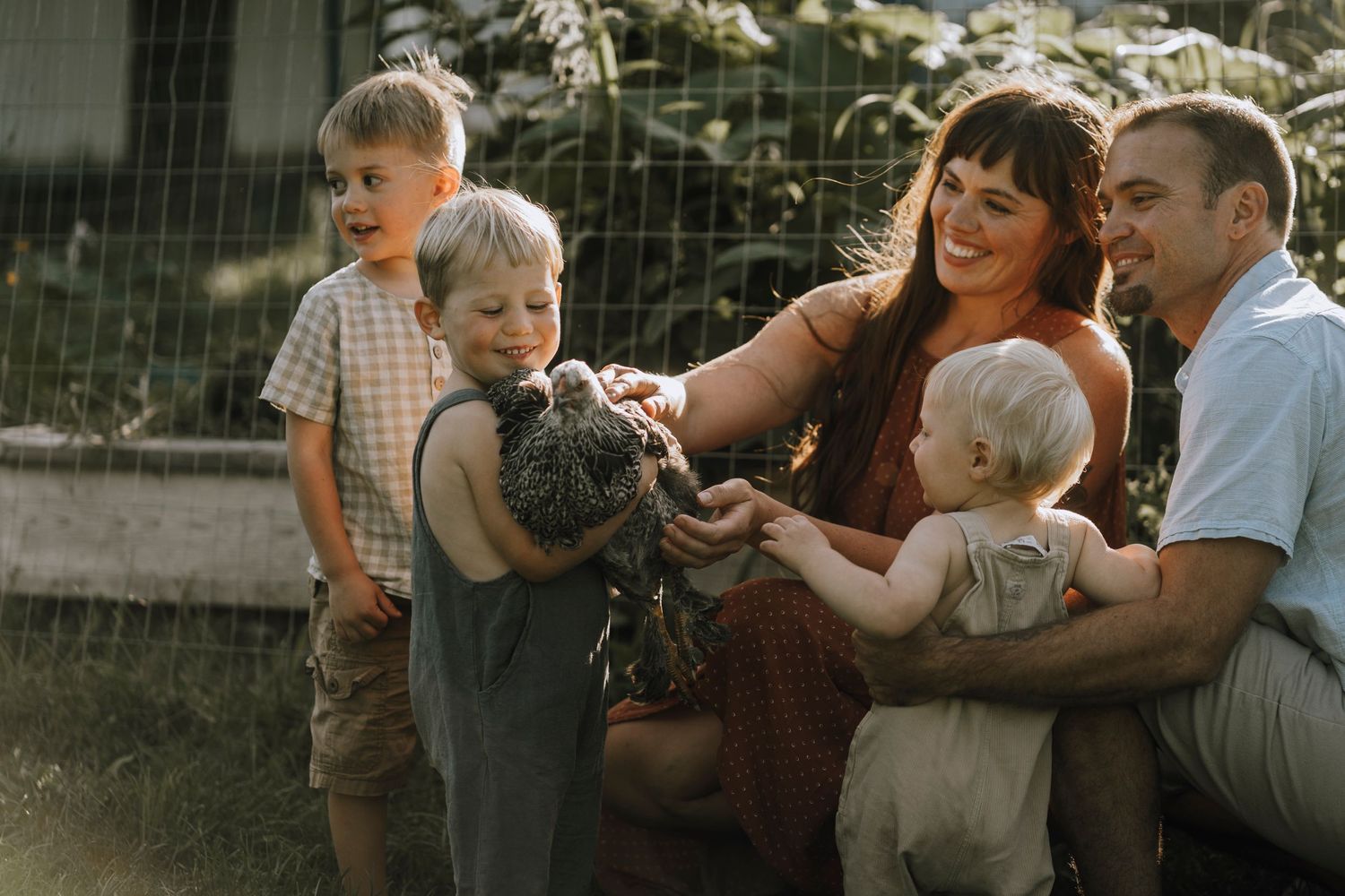 Family gathering outdoors with children exploring and interacting with farm animals.