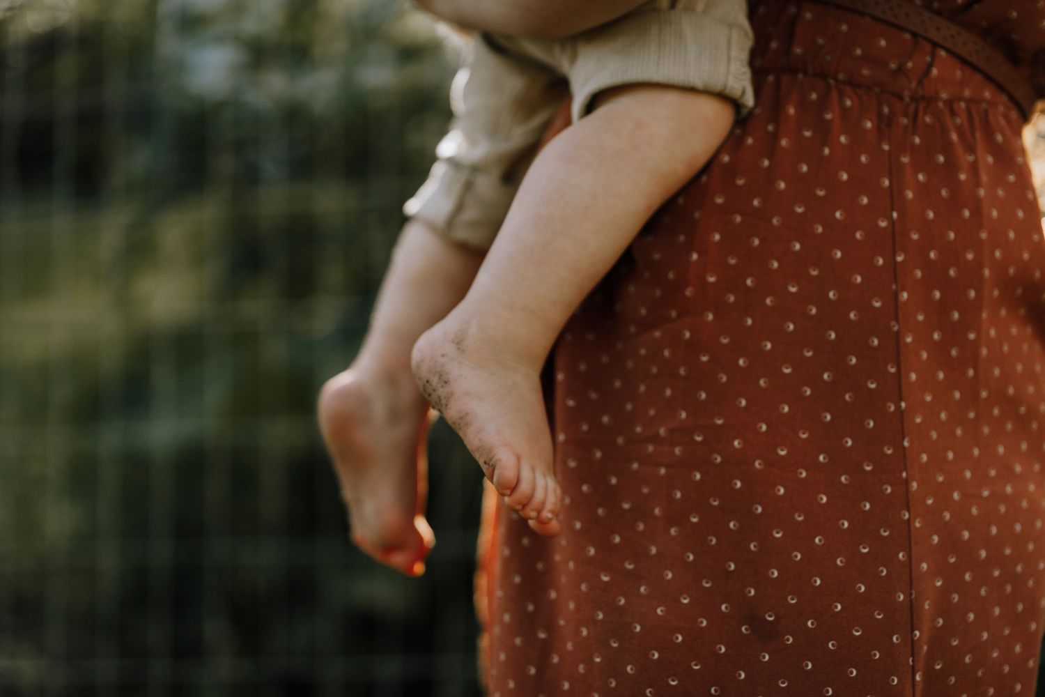 Close-up detail of polka dot dress and small child's legs being held.