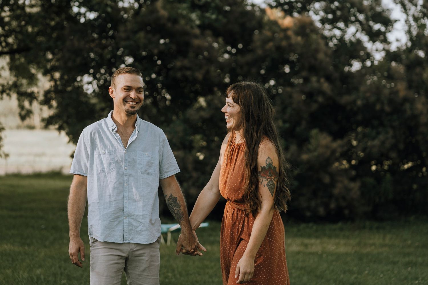 Couple walking hand in hand through a sunny park in summer clothing.