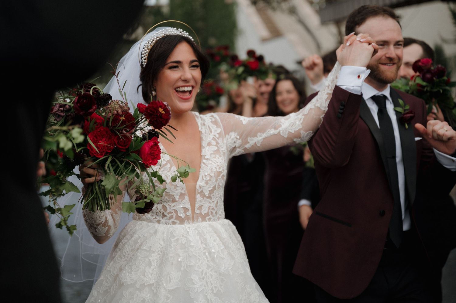 Joyful wedding celebration moment with white lace dress and burgundy florals.