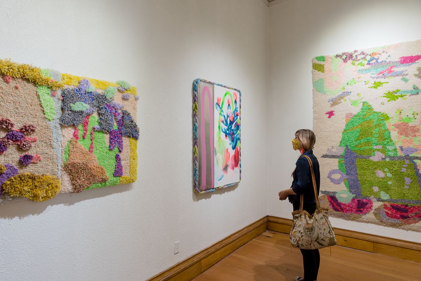 Visitor observing colorful abstract artwork displayed in a white-walled gallery space.